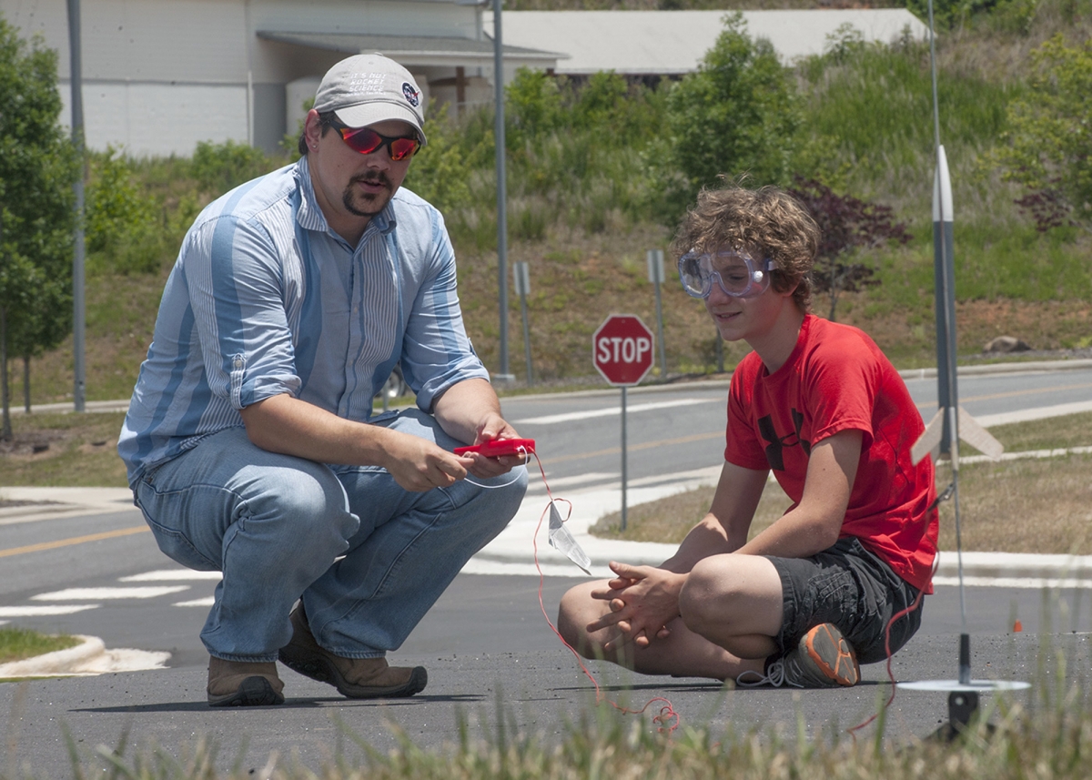 SCC instructor demonstrates how to use a launching contraption as a STEM camp student listens.