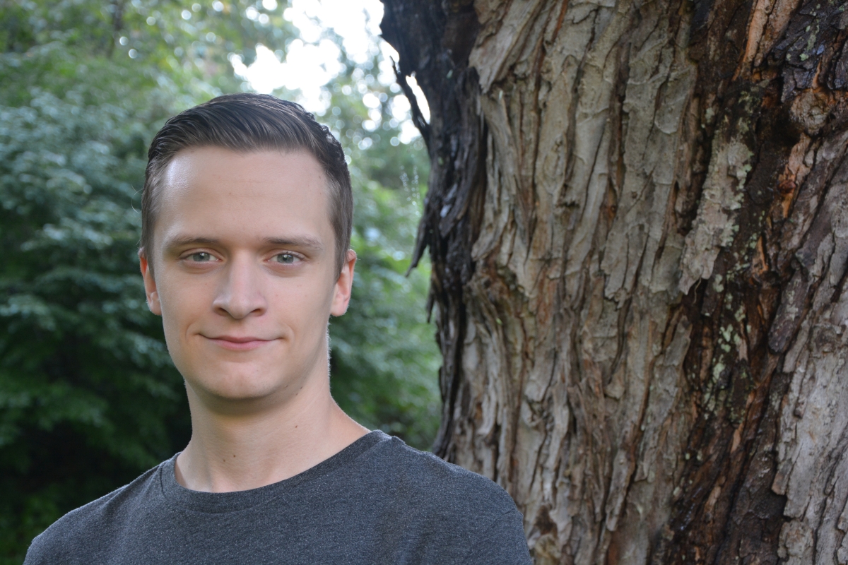 A young man smiles underneath a tree outside