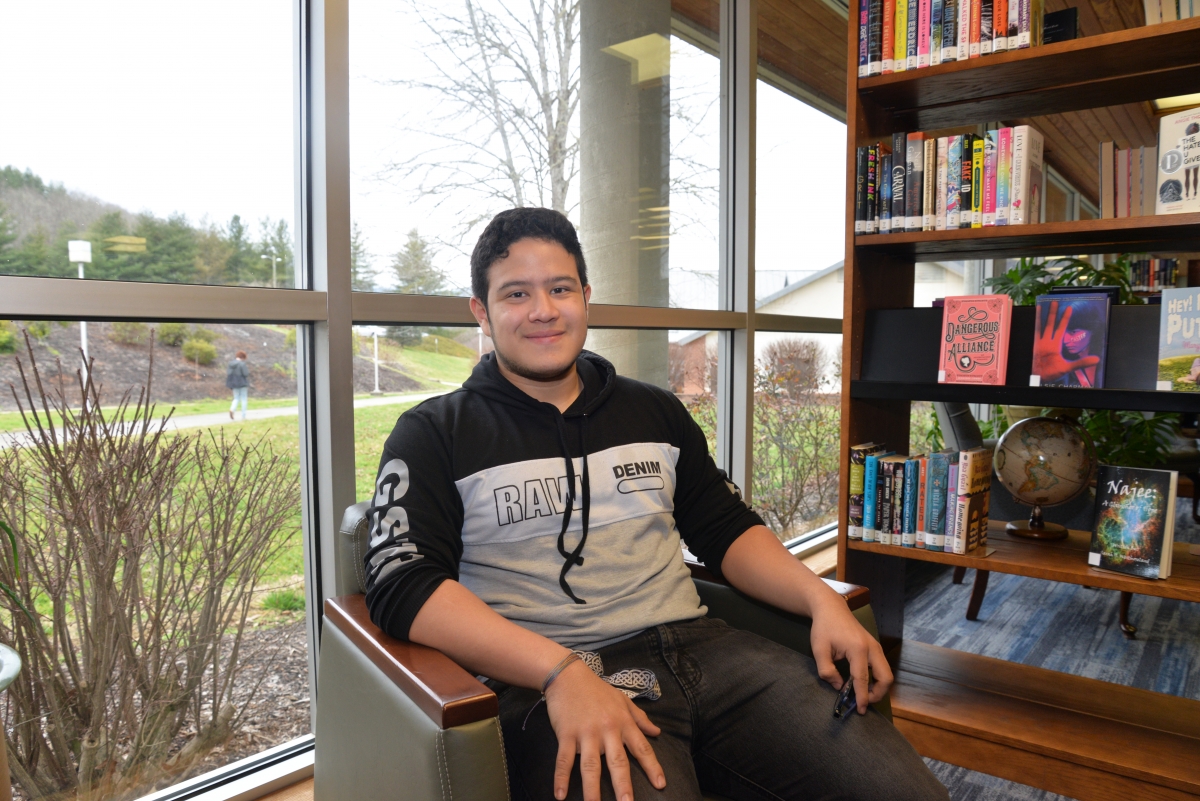 Young man smiles while sitting in front of a window at a library