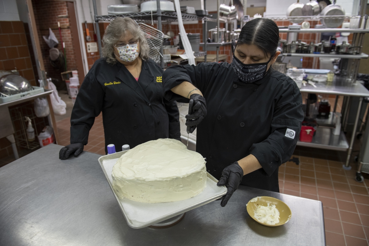 A female chef instructor watches a female student making a cake