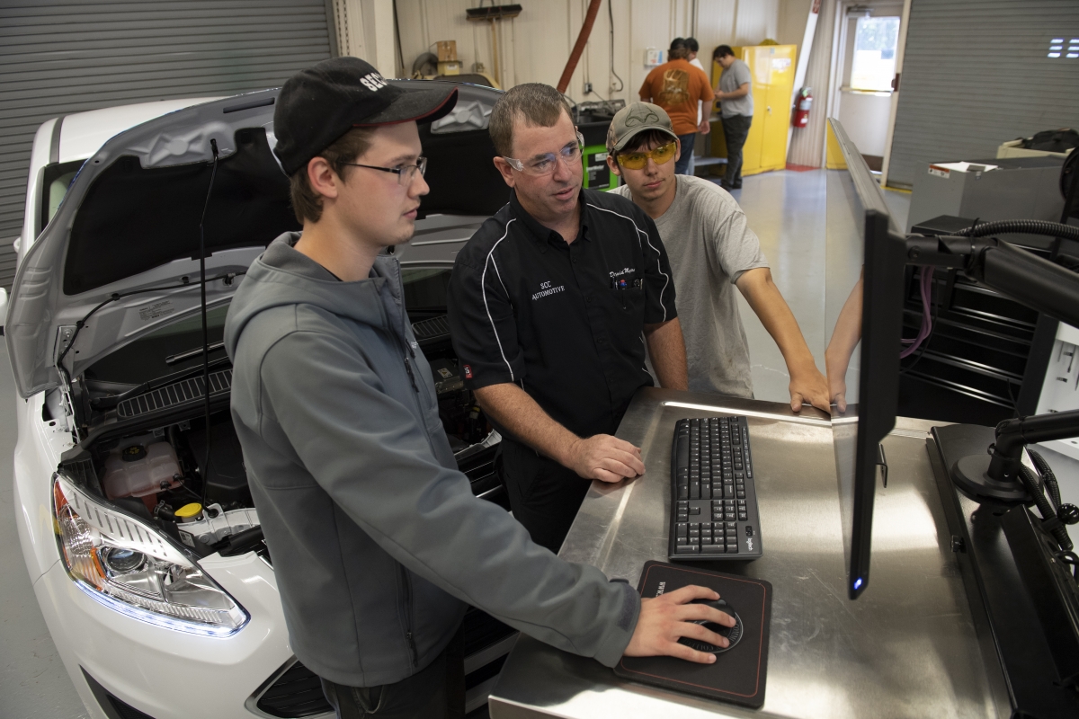 An automotive instructor works alongside students to analyze a car using a computer