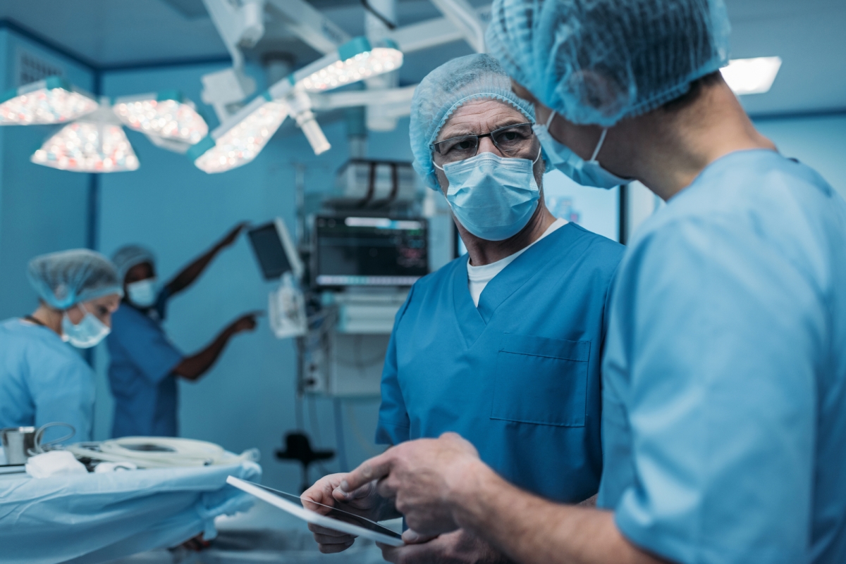 Two men in scrubs talk above an operating table