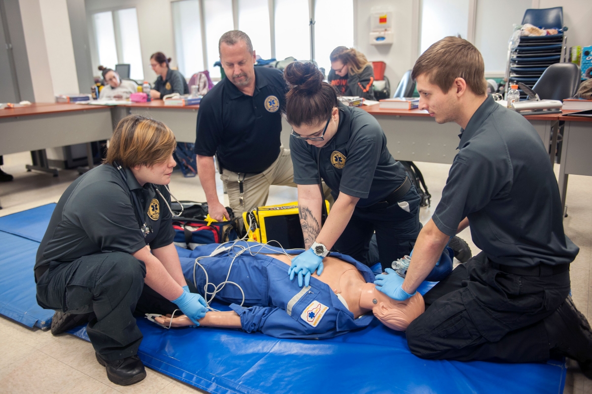 A group of EMS students practice on a simulation mannequin while their instructor observes