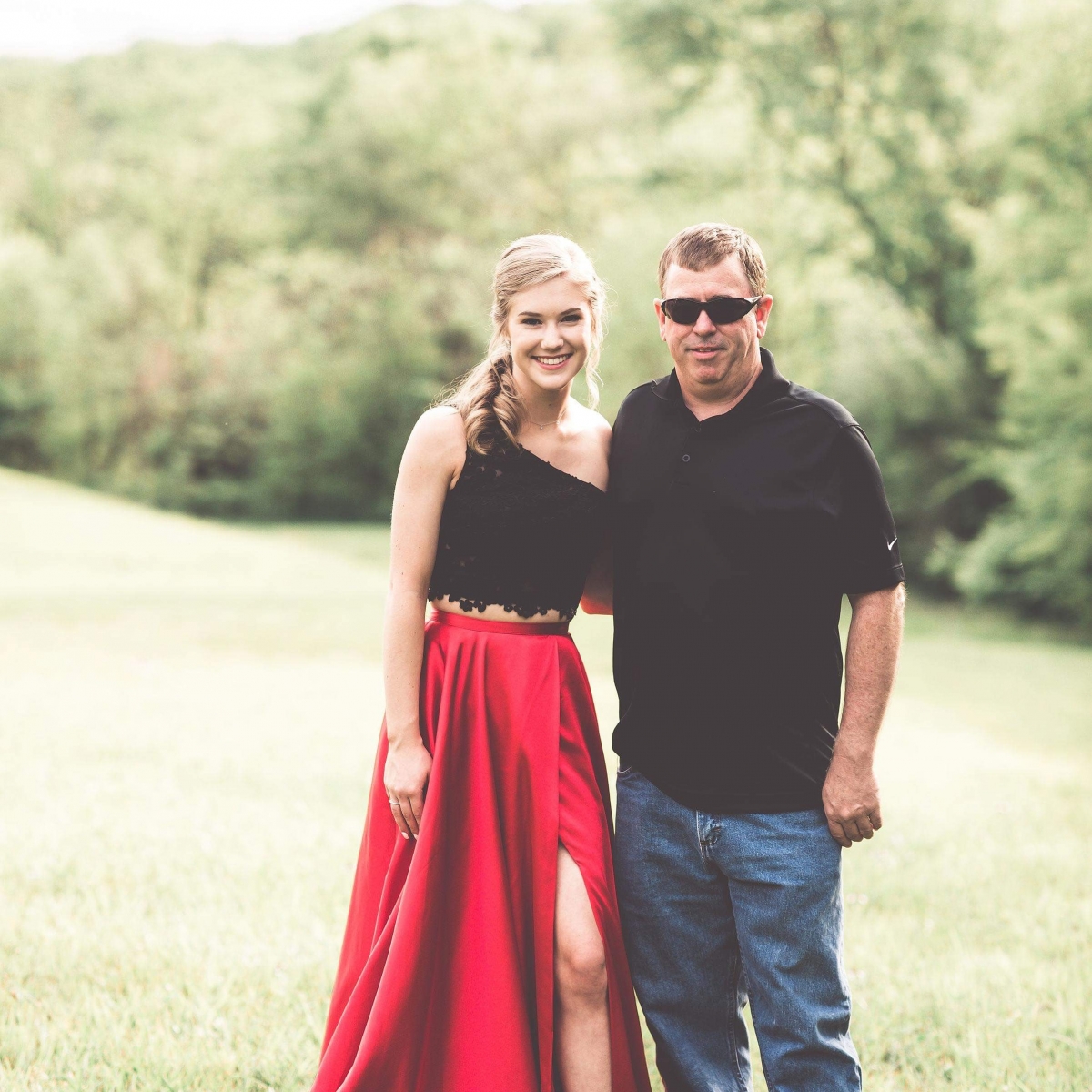 A young woman smiles in a beautiful dress while posing for a picture with her father