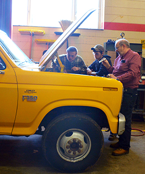 Photo of Bobby Price (right) and students Ryan Younce (left) and Jesse Peavy examine an engine in Franklin High School’s automotive lab.