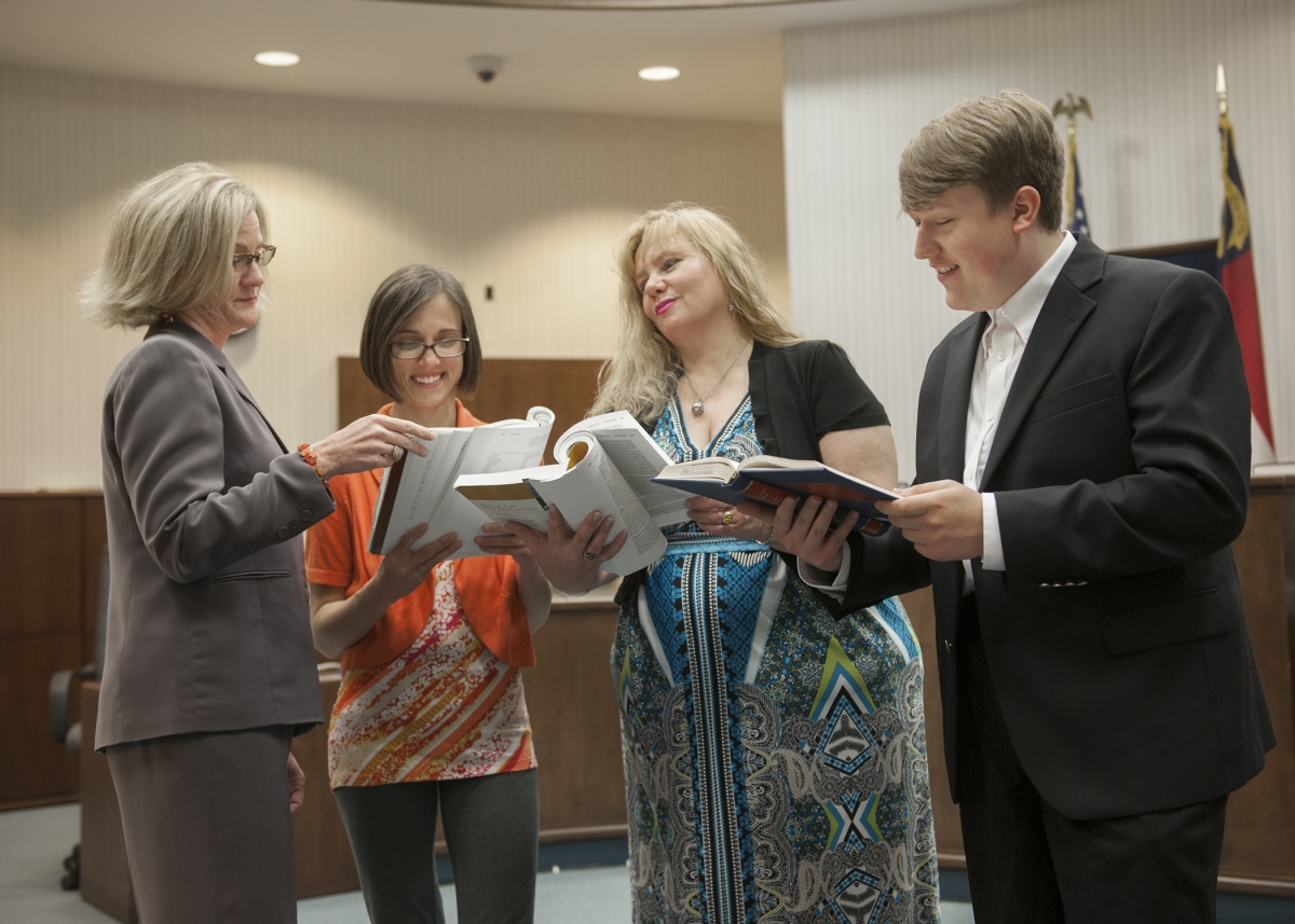 Female attorney stands with her students and reads legal books in a local court room.