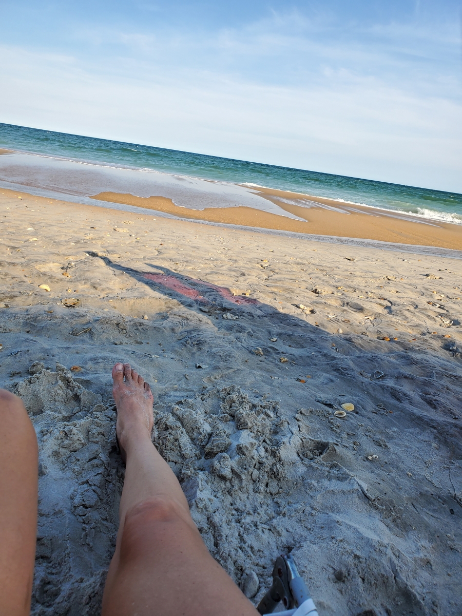 A woman laying with her feet in the sand at the beach.