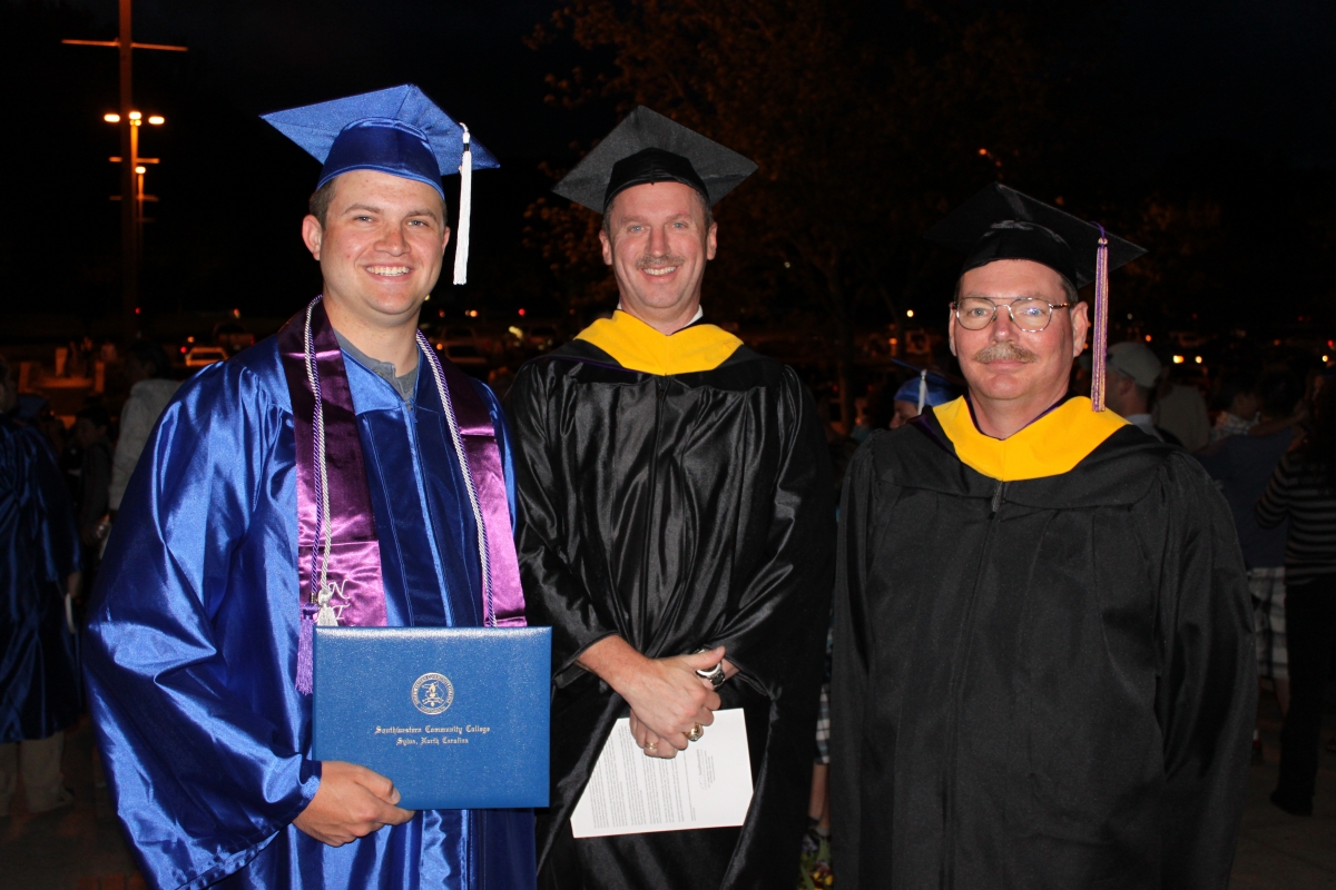 Graduate and two faculty members pose outside at night