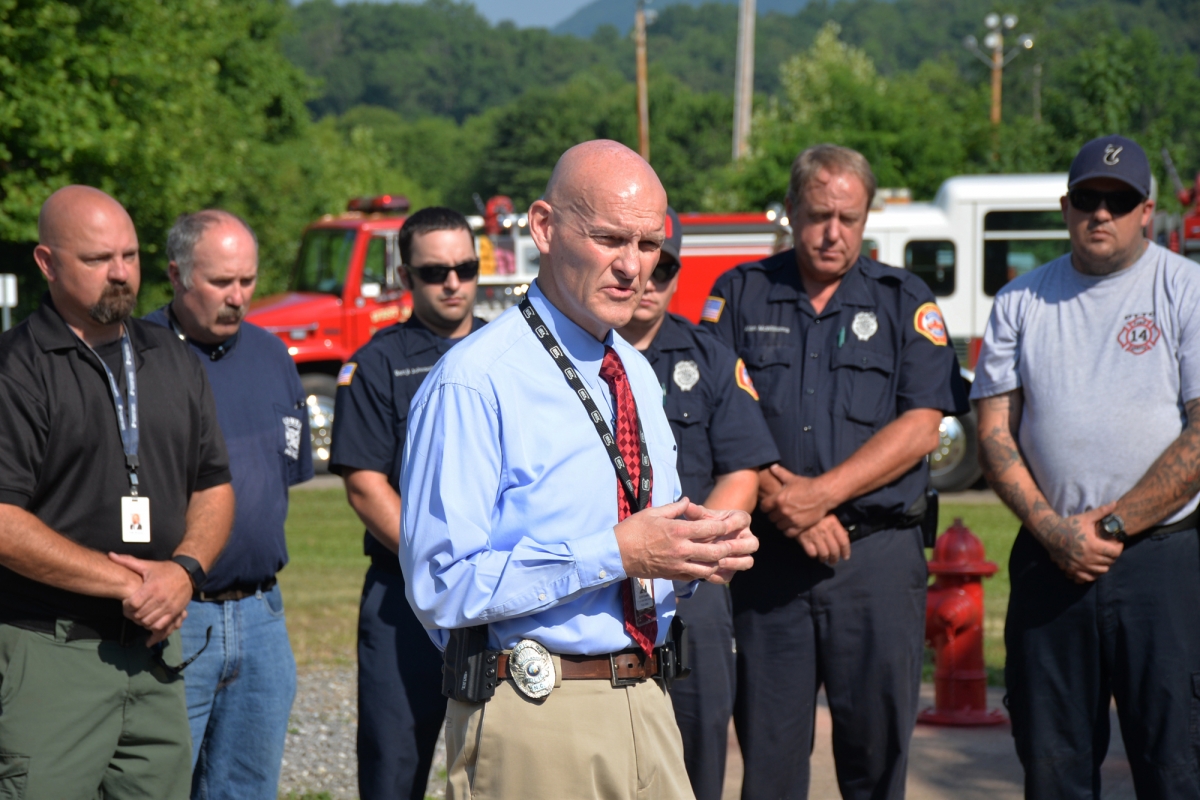 Curtis Dowdle speaks; first responders and emergency vehicles are in the background
