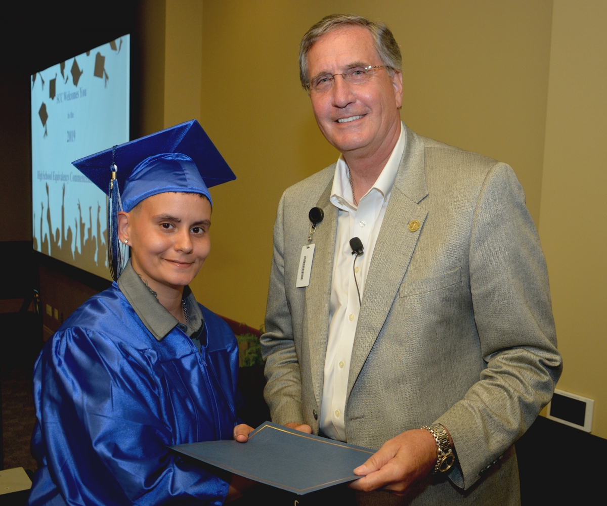 Student wearing graduation cap and gown accepts diploma from college president