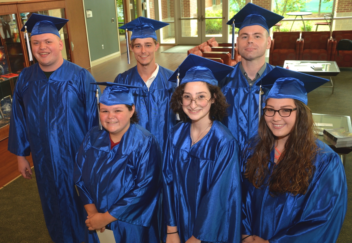 Six students pose wearing their graduation caps and gowns