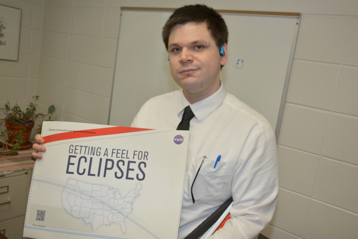 Man holds up a book cover entitled "Getting A Feel For Eclipses"