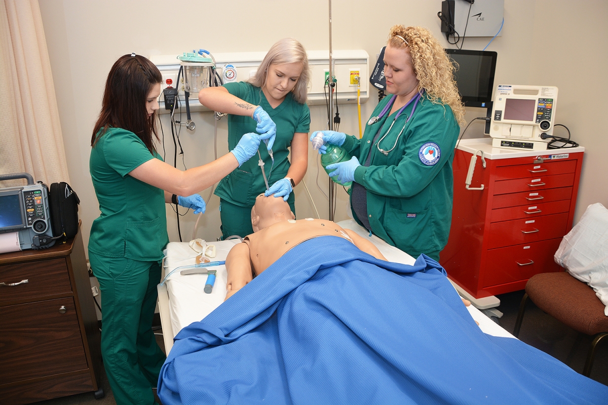 Three female students wearing scrubs practice their respiratory therapy skills on a mannequin inside a room on SCC's Jackson Campus.