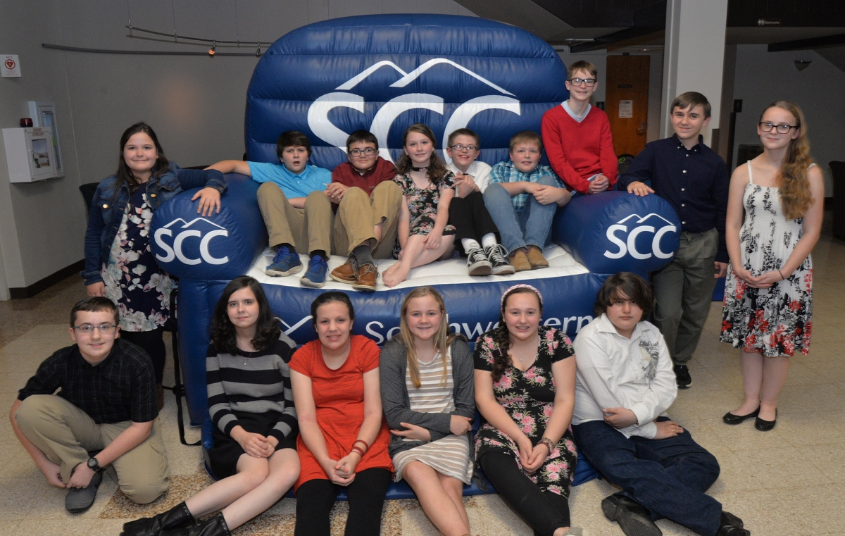 More than a dozen students pose on a blue inflatable chair with white SCC logos.