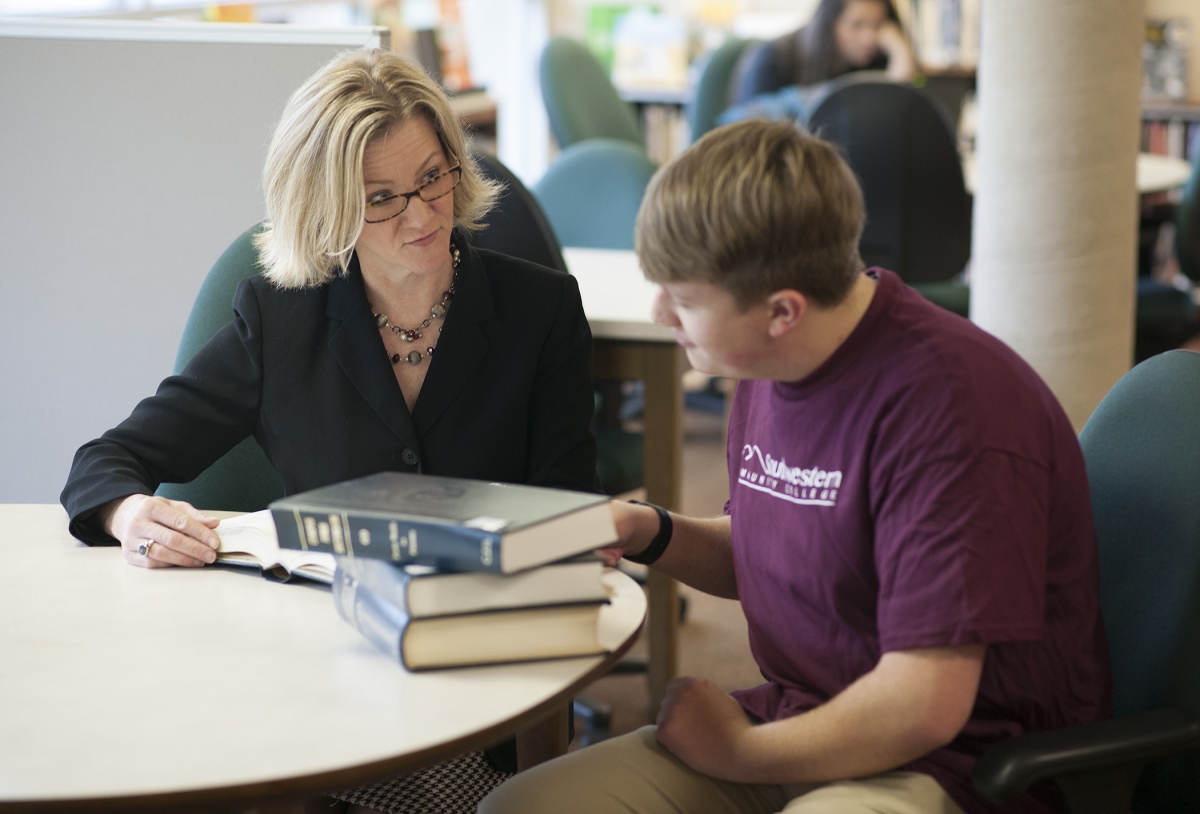 Sitting a library desk, a college instructor reviews court documents with a student.