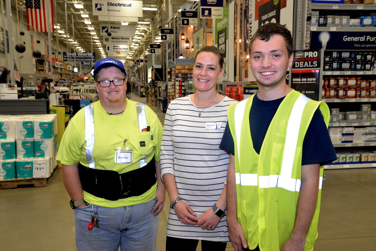 Two men and a lady pose indoors with Lowe's aisles and cash register lines in the background