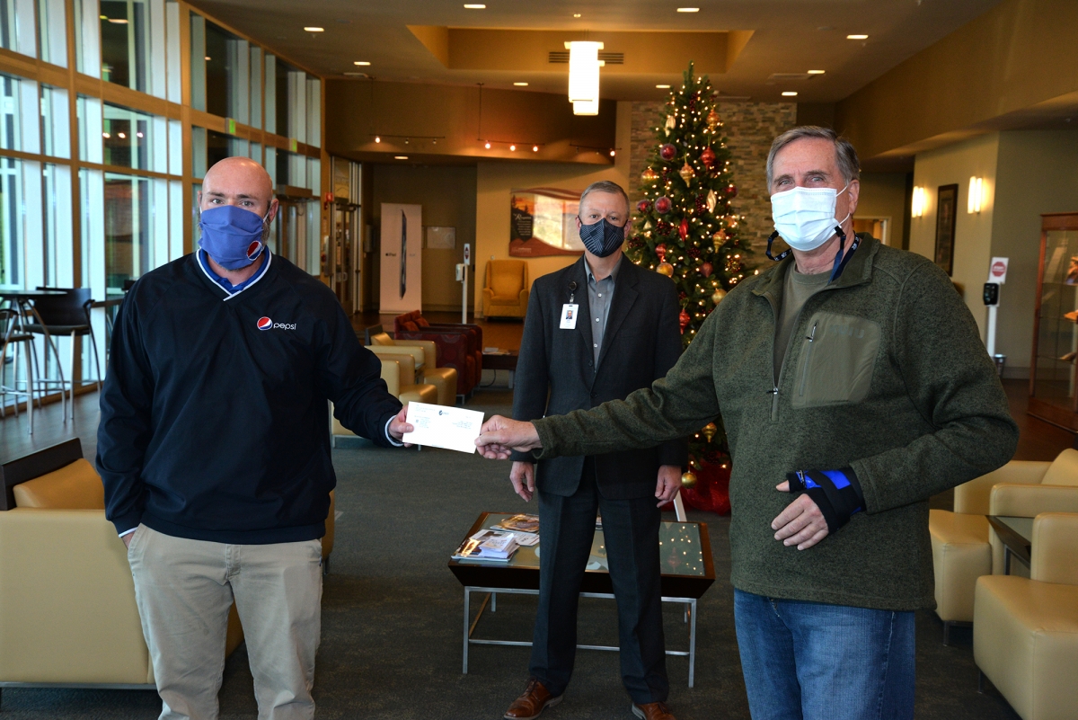 Two men hold a check while a third stands behind them. They are social distancing and wearing masks
