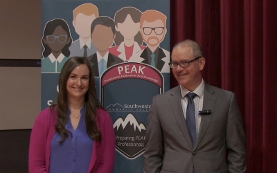 Man and woman stand in front of a PEAK banner.