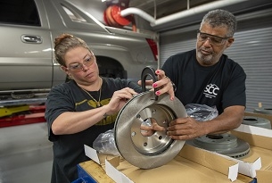 A man and a woman inspect a tired part in an automotive shop