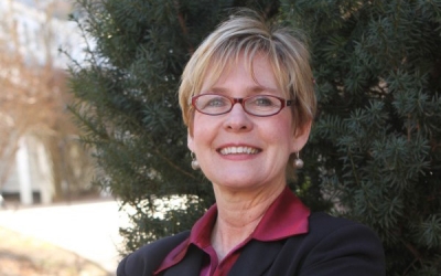 Lady stands outdoors in front of an evergreen tree.