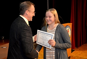 A young girl smiles as she accepts a certificate from a college leader