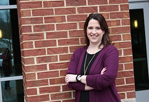 A woman in a cardigan smiles against a brick wall