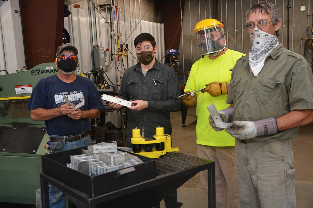 Men hold pieces of metal while wearing protective face gear