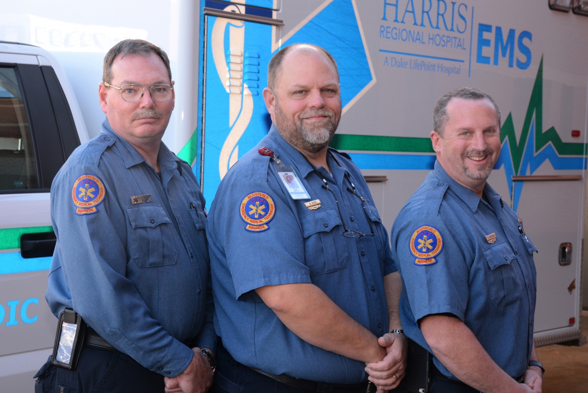 Three paramedics pose in front of a Harris Regional ambulance