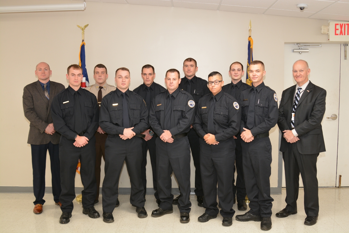 A group of law enforcement graduates huddle together for a group pictures with their instructors.