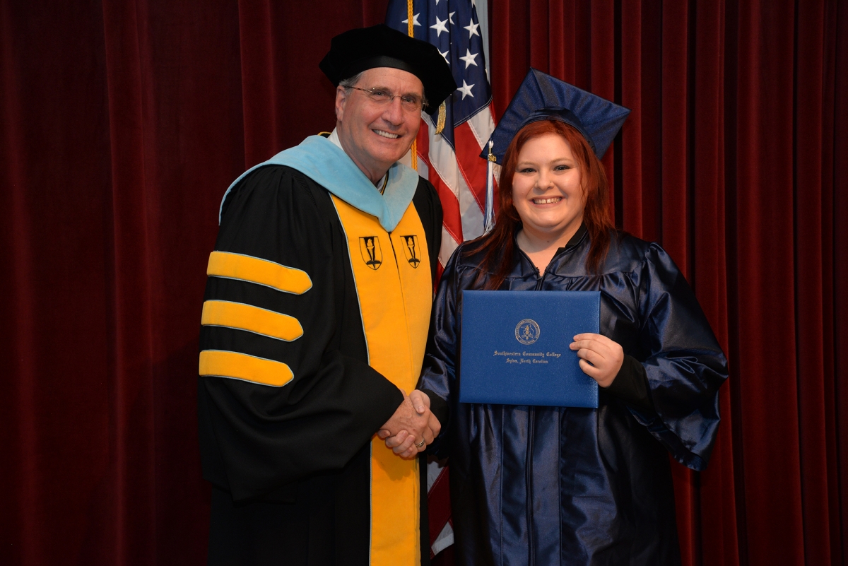 A young woman shaking hands with a college president as she receives a certificate at a graduation ceremony.