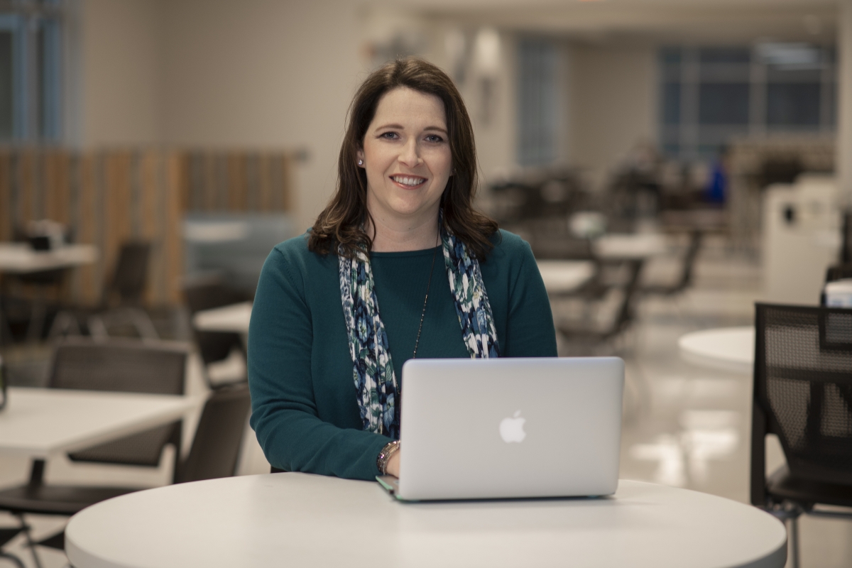 Young woman dressed in blue sits behind a laptop at a table