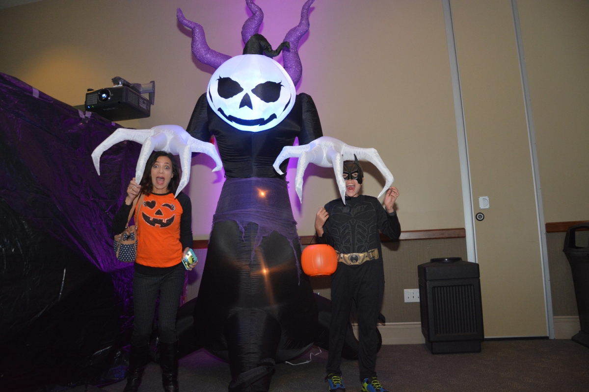 Two trick-or-treaters pretend to be frightened as an inflatable pumpkin monster lowers its hands over their heads.