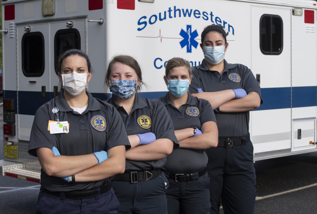 A group of female EMS students stand in a line wearing masks while crossing their arms