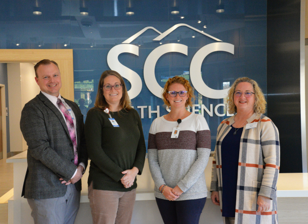 Four individuals stand in front of SCC's logo