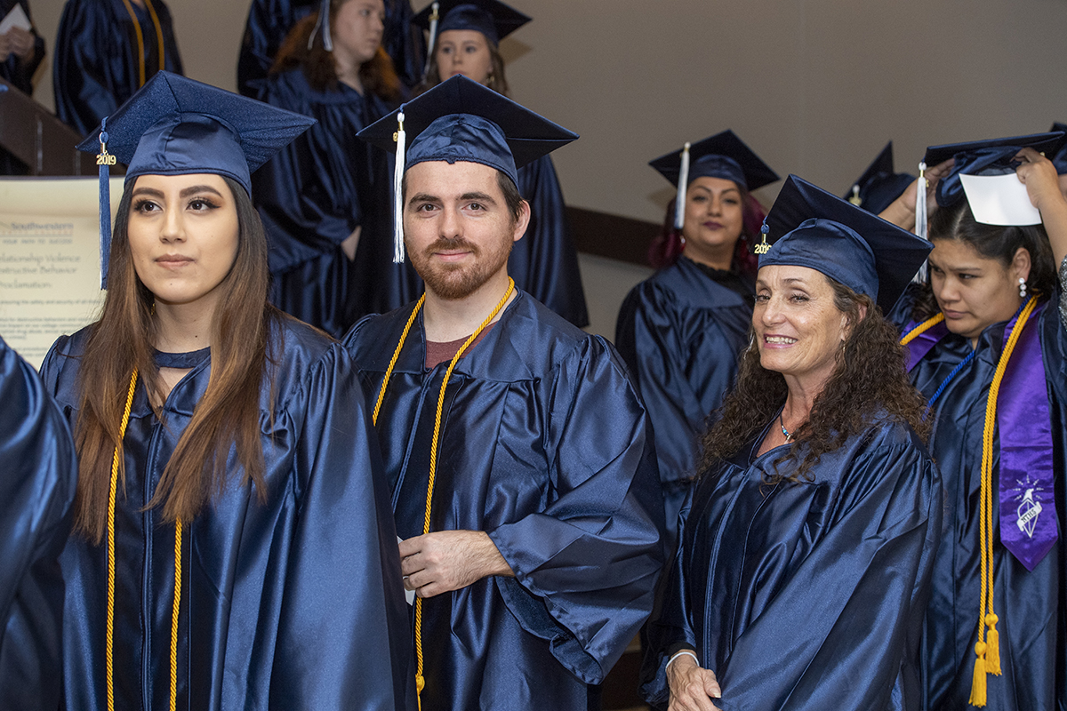 A group of students lined up a staircase and smile as they prepare to enter an auditorium.