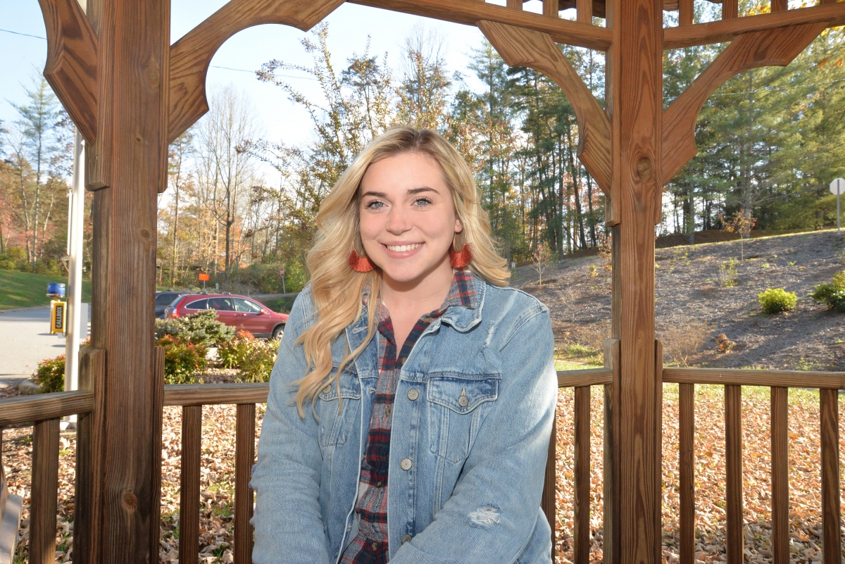 Young blonde woman smiles underneath a gazebo on a sunny fall day.