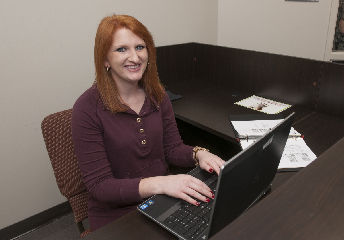 A young woman smiles while typing on a laptop