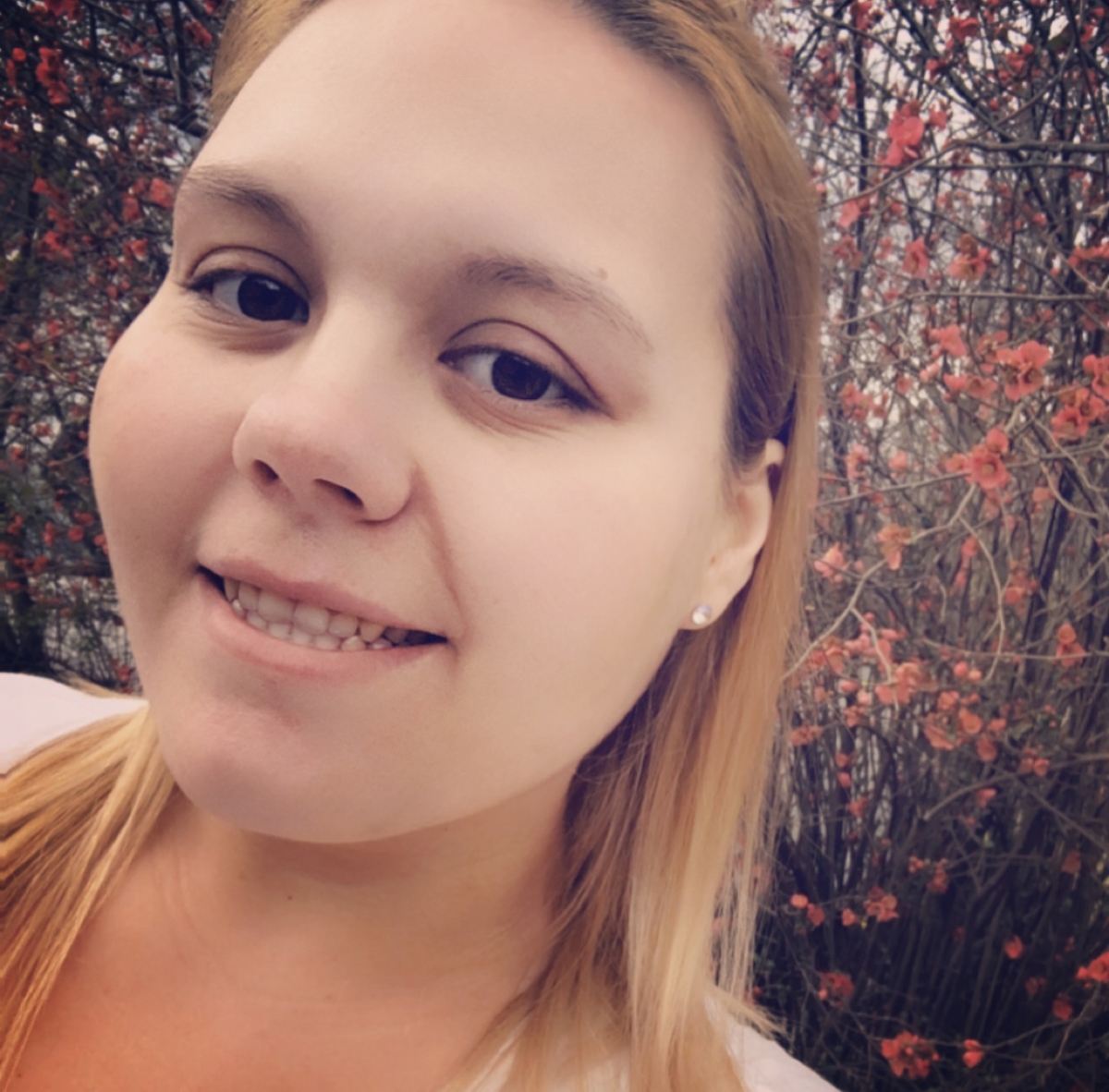 A young woman smiles for a selfie while surrounded by flowers