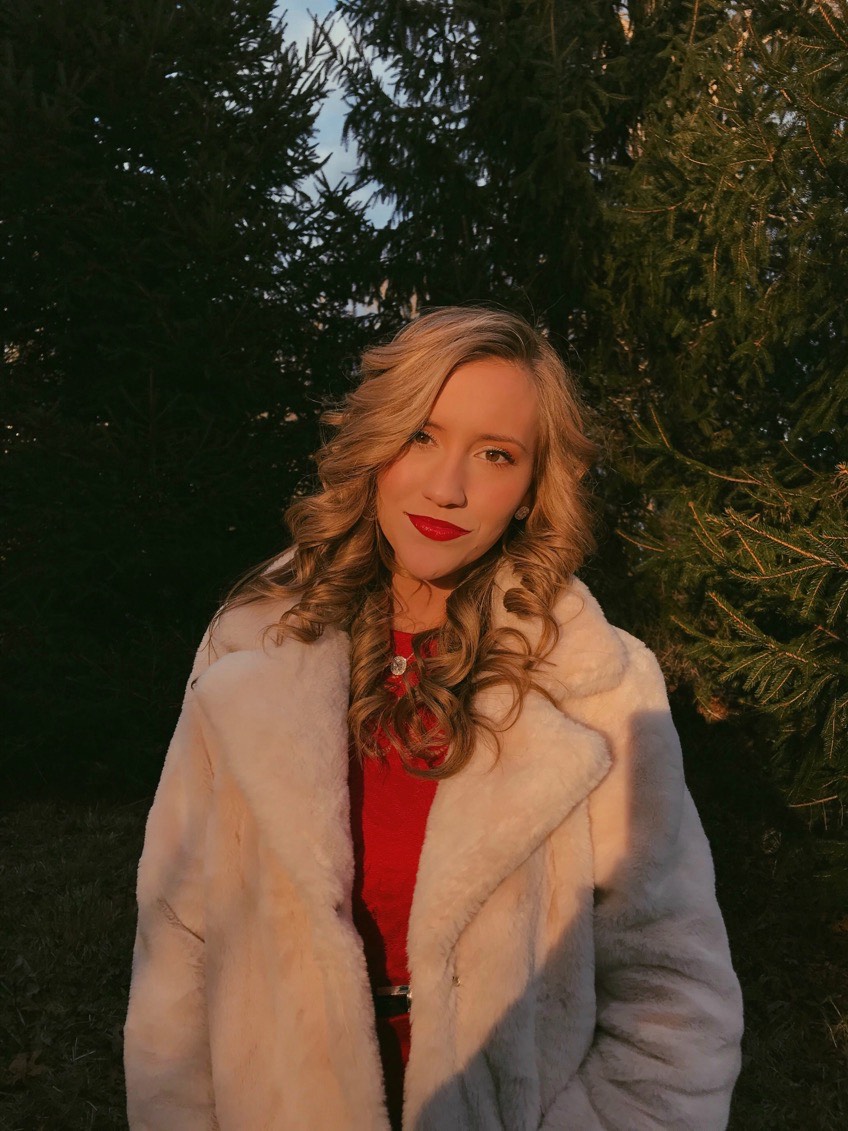 A young woman with blonde hair and red lipstick stands outside for a picture