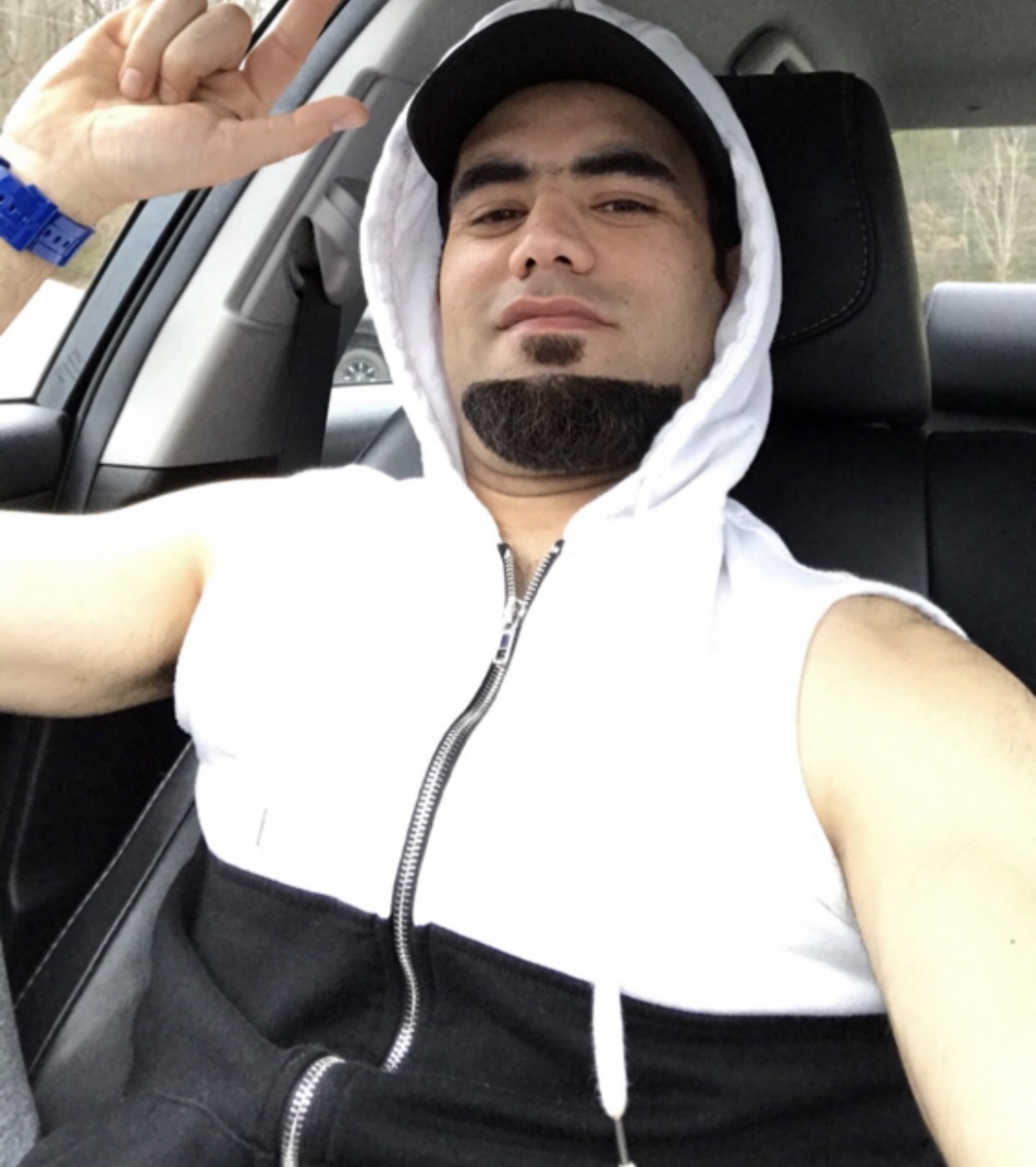 Young man in hoodie sits in his car throwing up playful hand gesture.