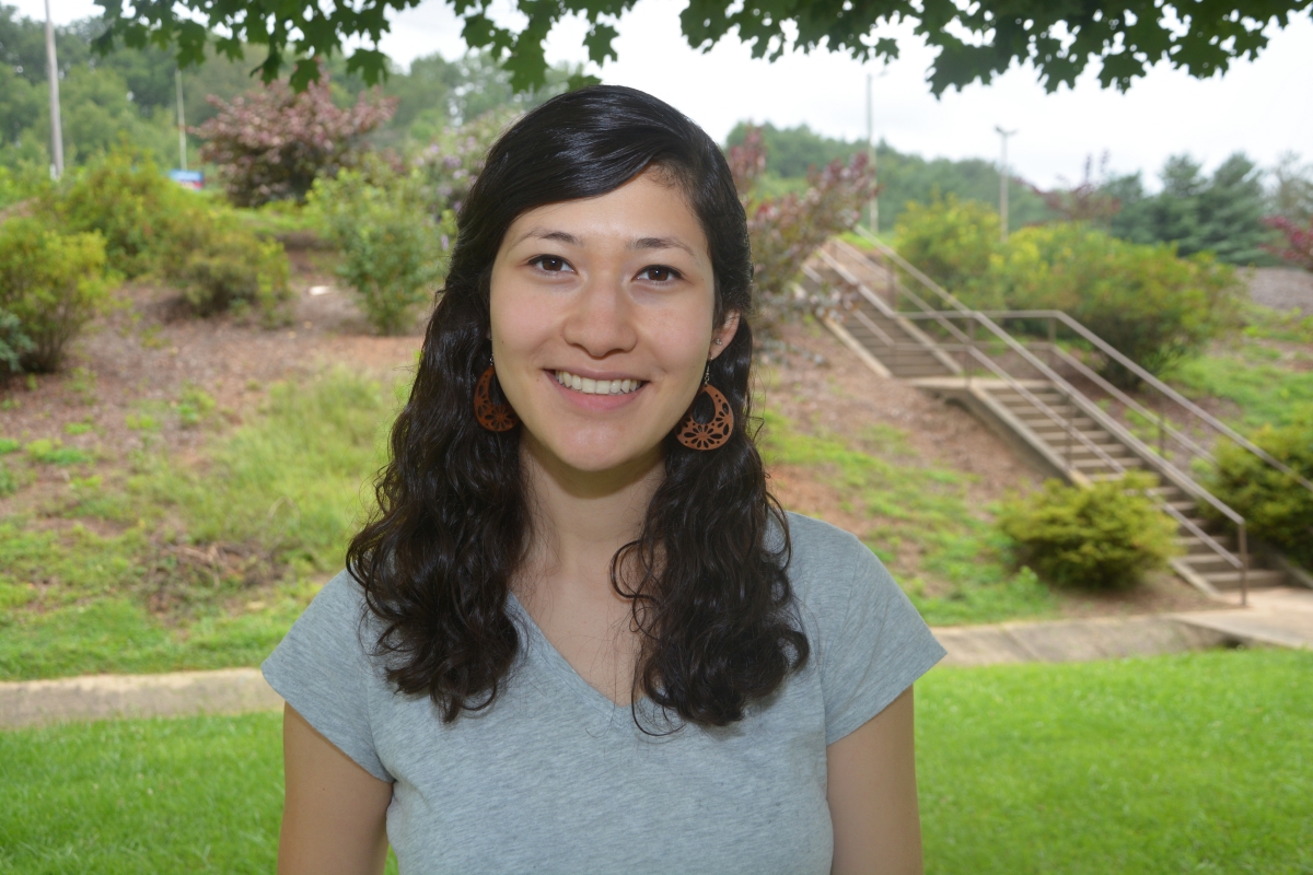 A young woman with black hair smiles under a tree on a foggy morning