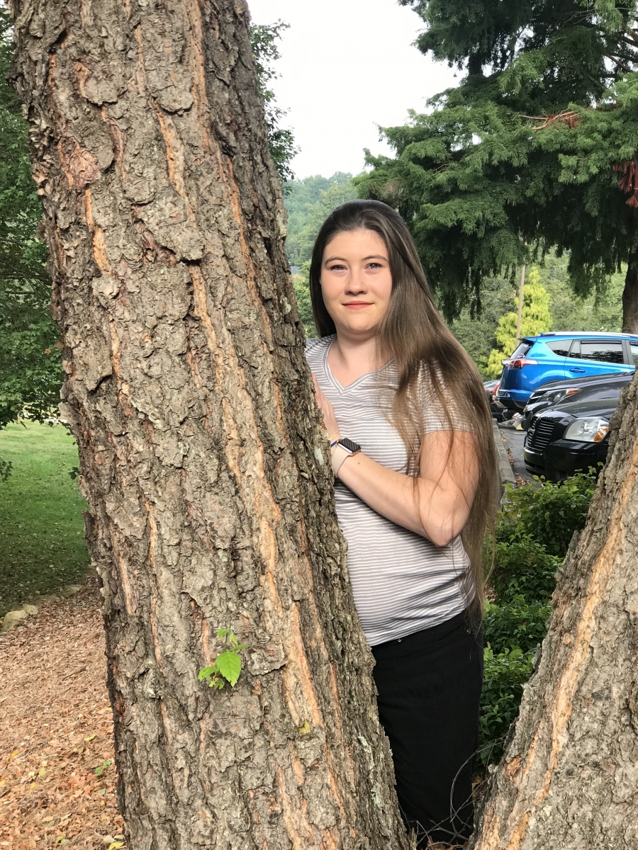Young woman stands outside against a tree.