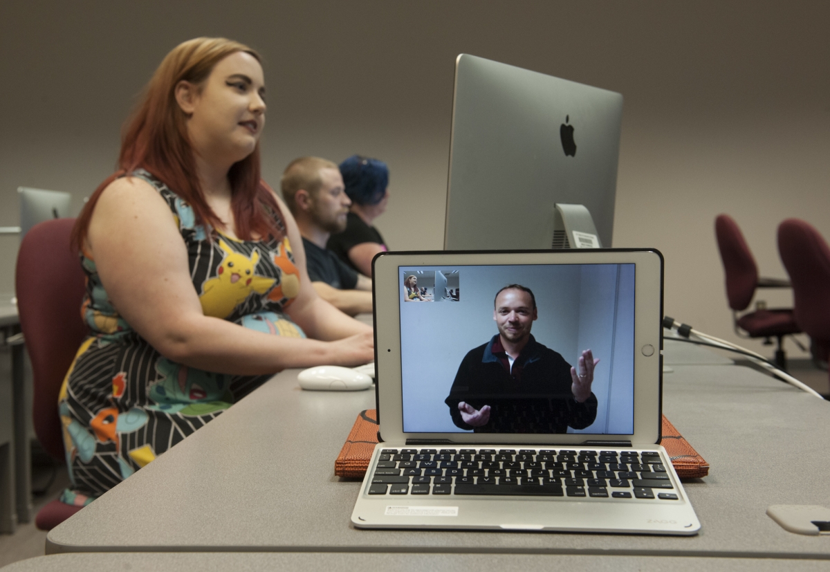 A young woman is working on a computer while an instructor is video chatting the class from an ipad