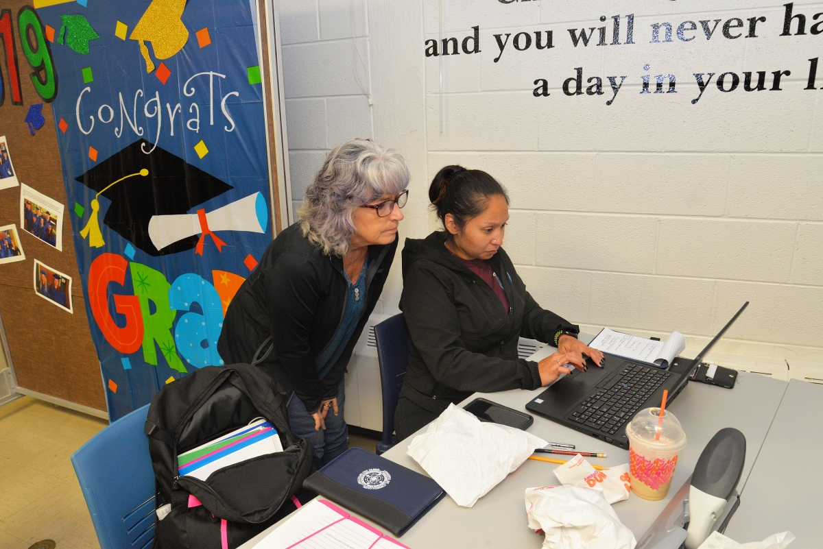 Female instructor assist young female student working on a laptop.