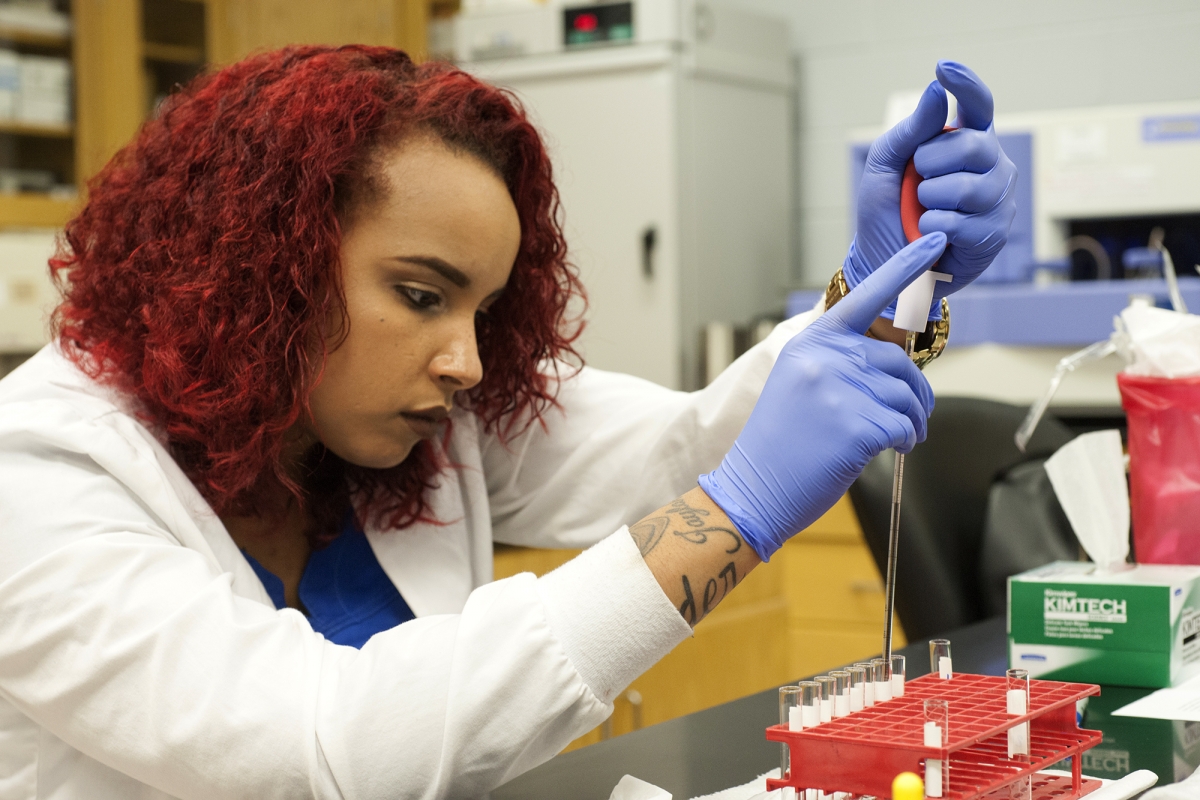 Student in lab coat performs a test using lab equipment.