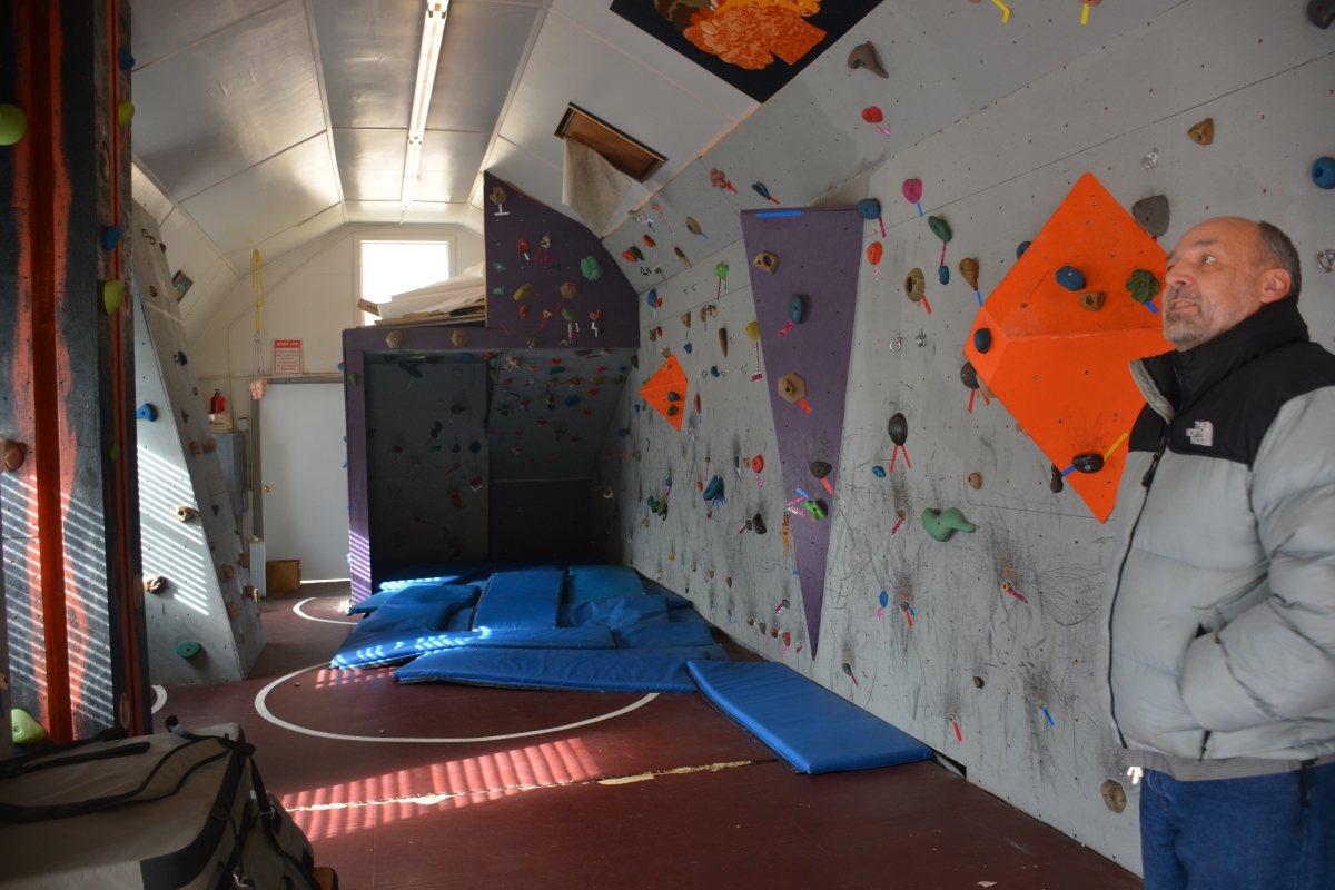 Man stands beside an indoor rock climbing wall.