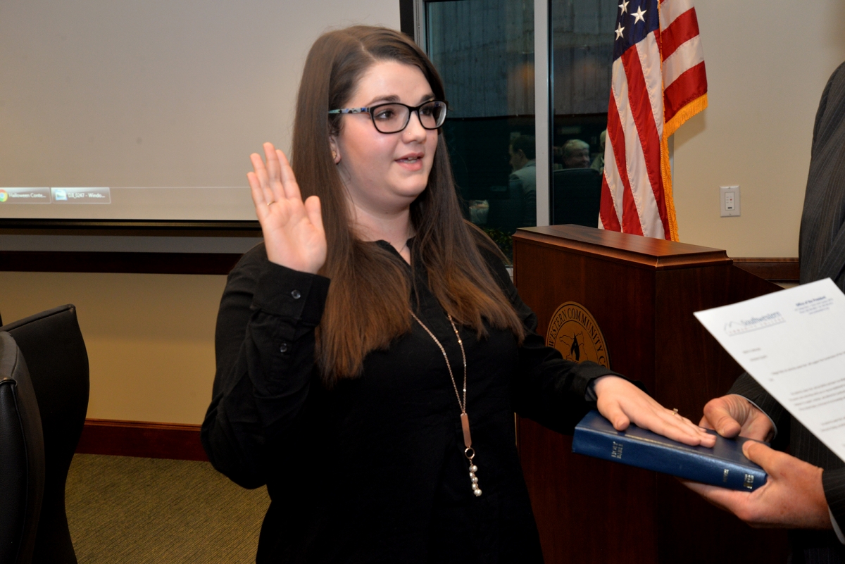 Young lady places a hand in the air and the other on a Bible.