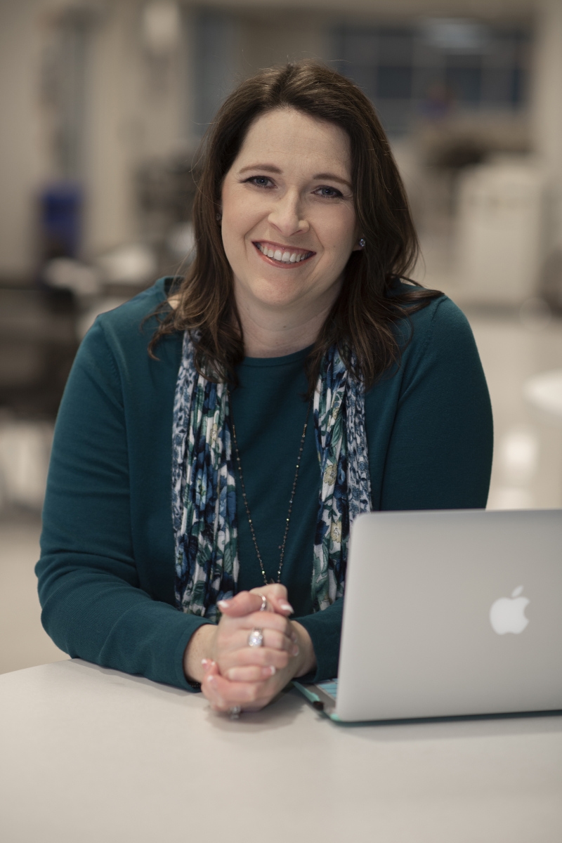 Woman sits next to laptop and smiles