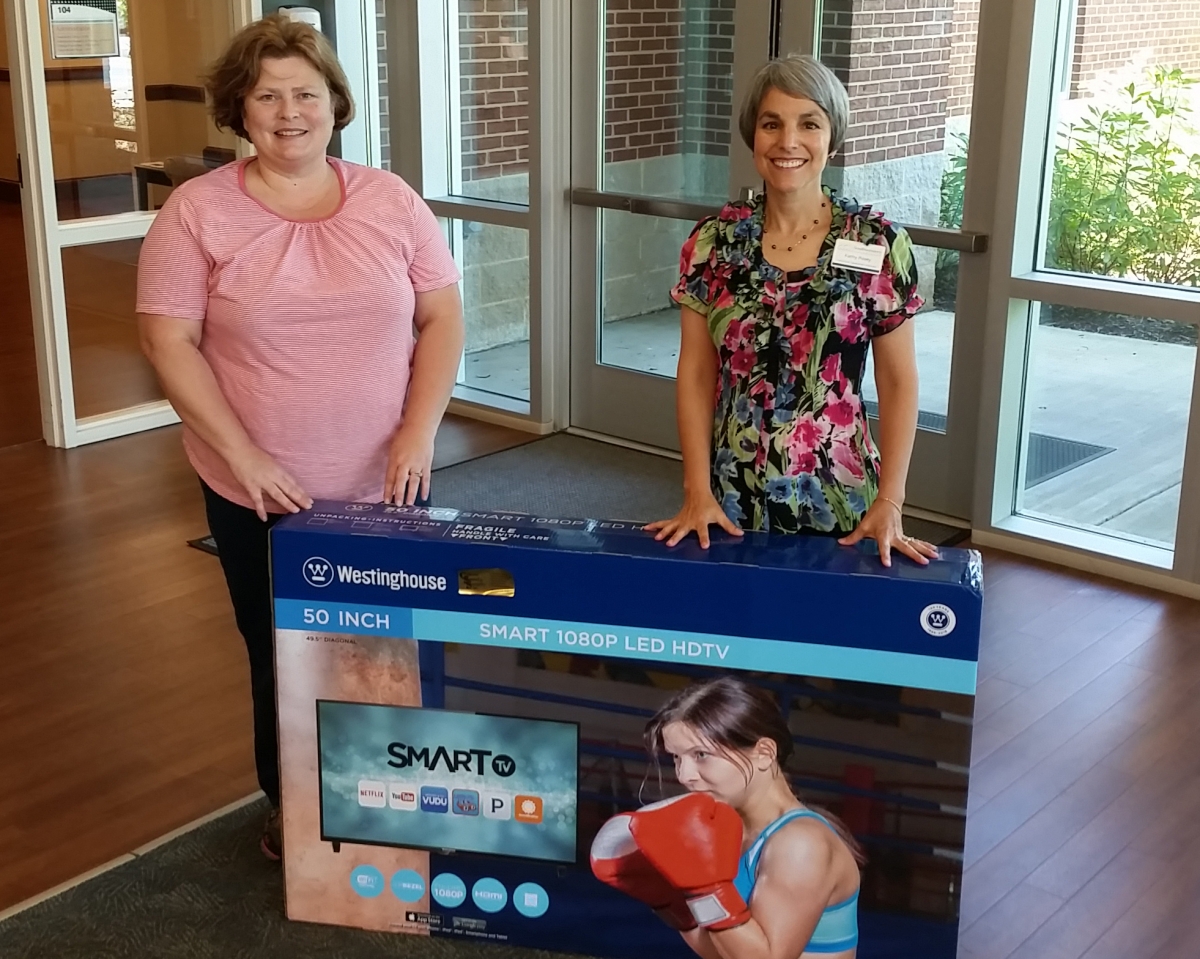 Two ladies stand beside a flat screen TV.