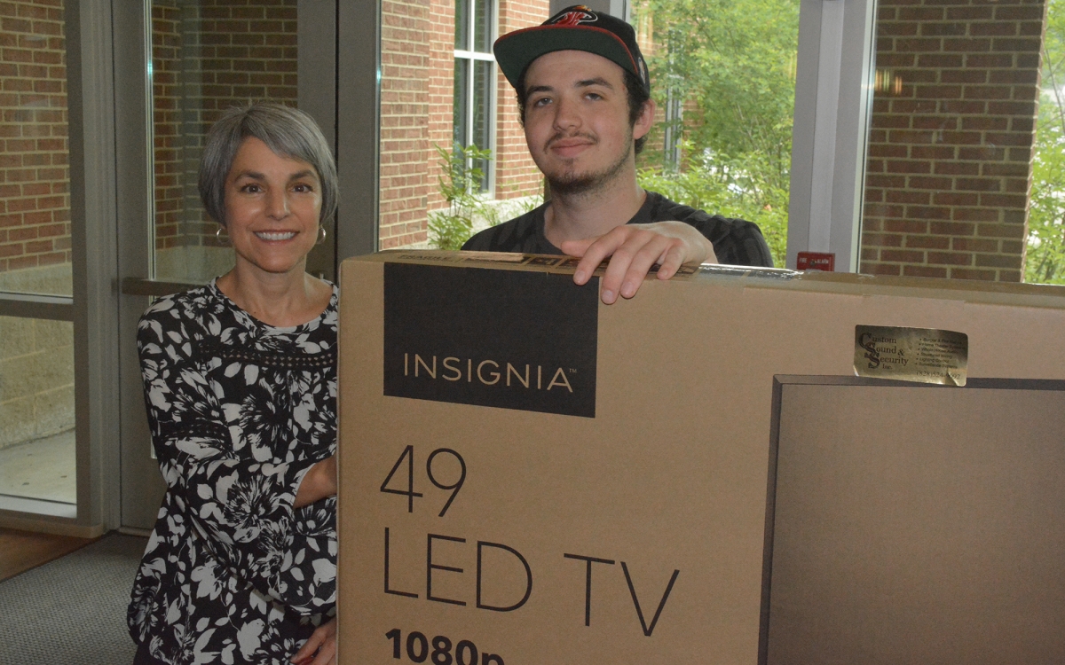 Man and woman hold a cardboard box that contains a flat-screen TV.